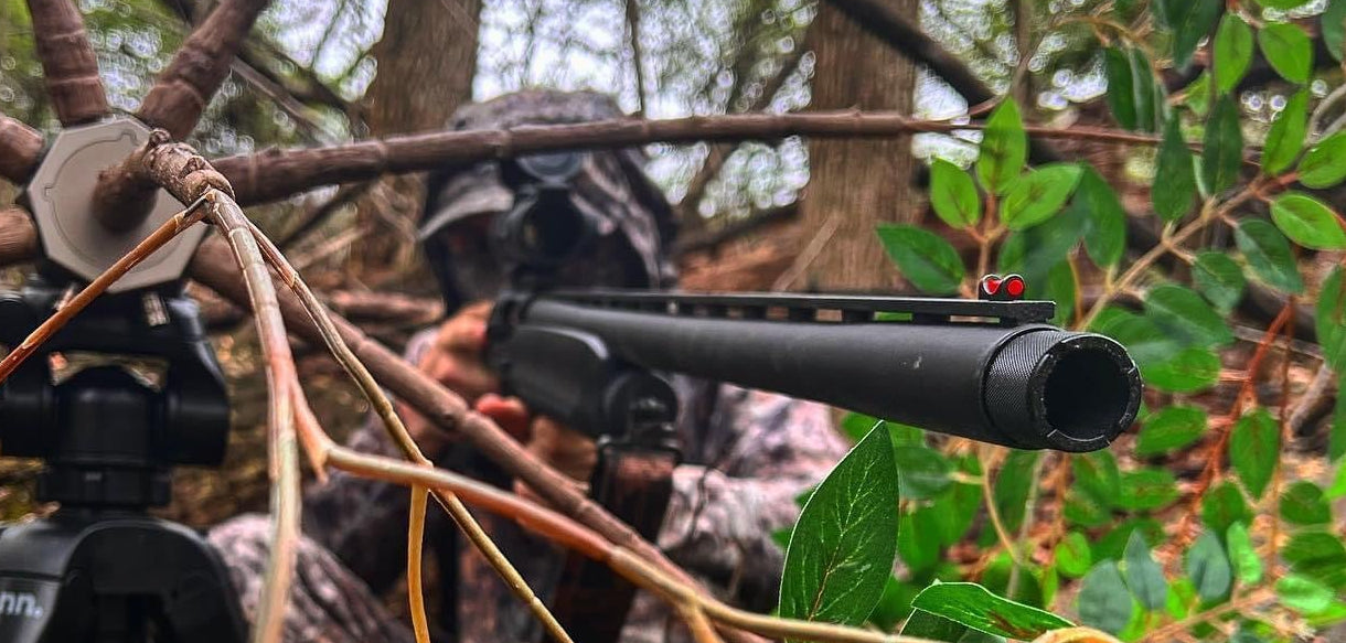 Hunting scene with a rifle and camera setup in a forest.